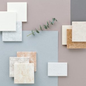 Stylish flat lay showcasing various marble and ceramic tiles on a muted background with a touch of greenery.